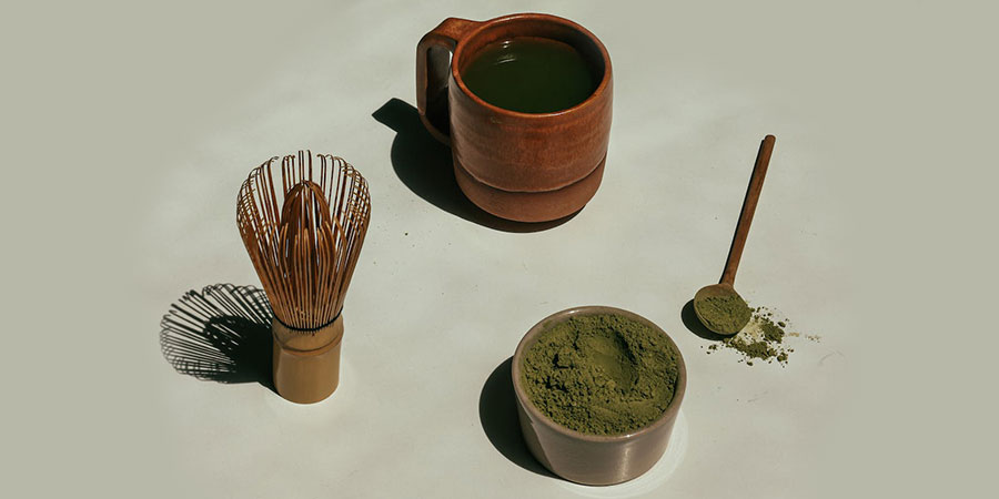 cup of green tea, whisk, green colored powder and a teaspoon